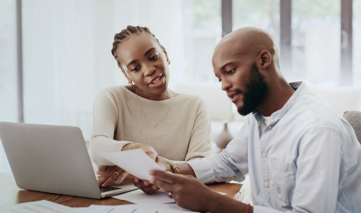 Couple looking at papers and laptop discussing whether to change their mortgage company.
