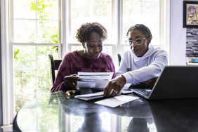 Two women paying bills and using a laptop at a kitchen table