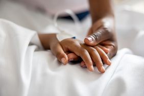 Adult holding a child's hand in a hospital bed